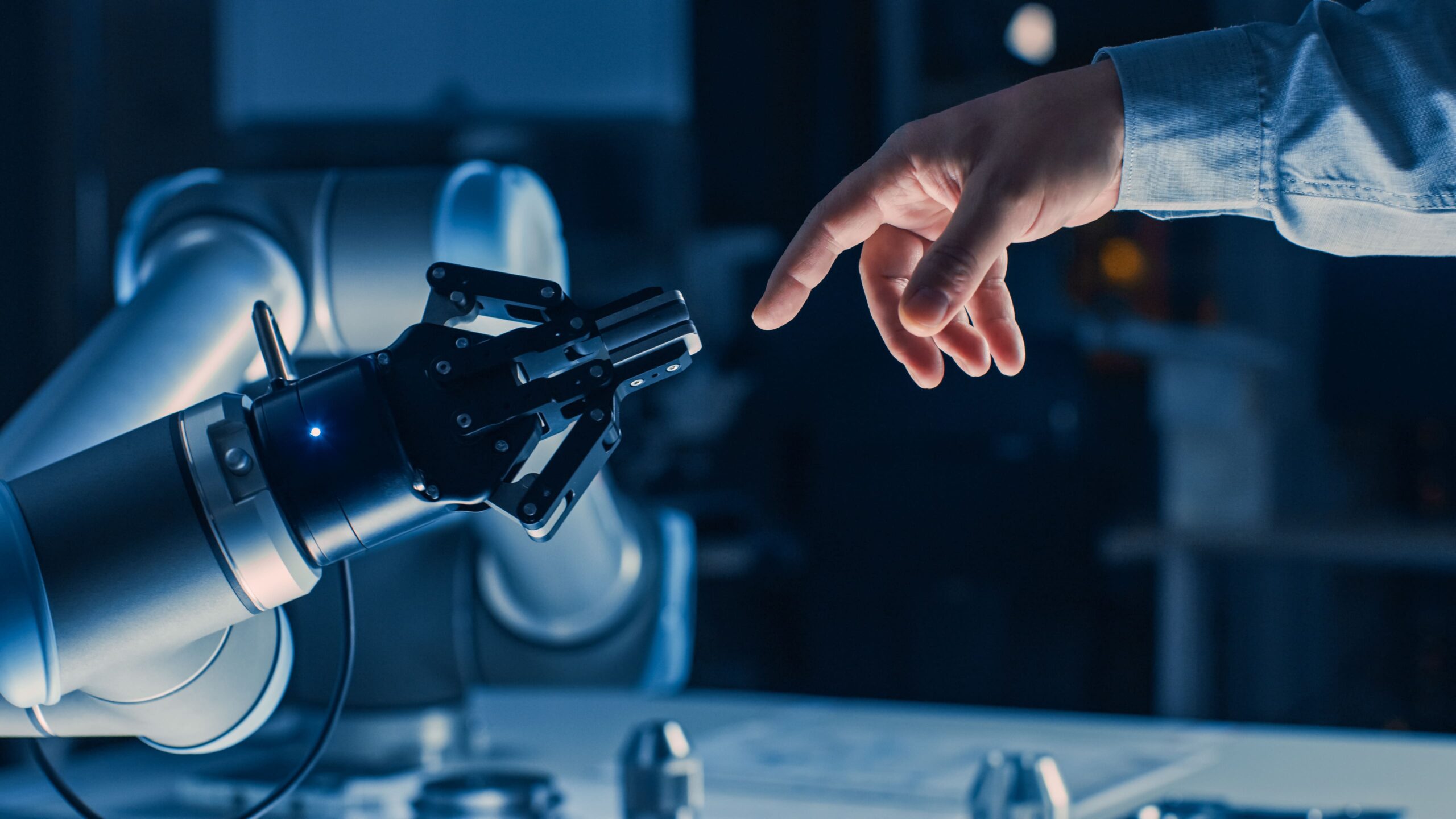Human hand reaching a robotic hand, symbolising open innovation, collaboration and digital transformation in modern manufacturing.