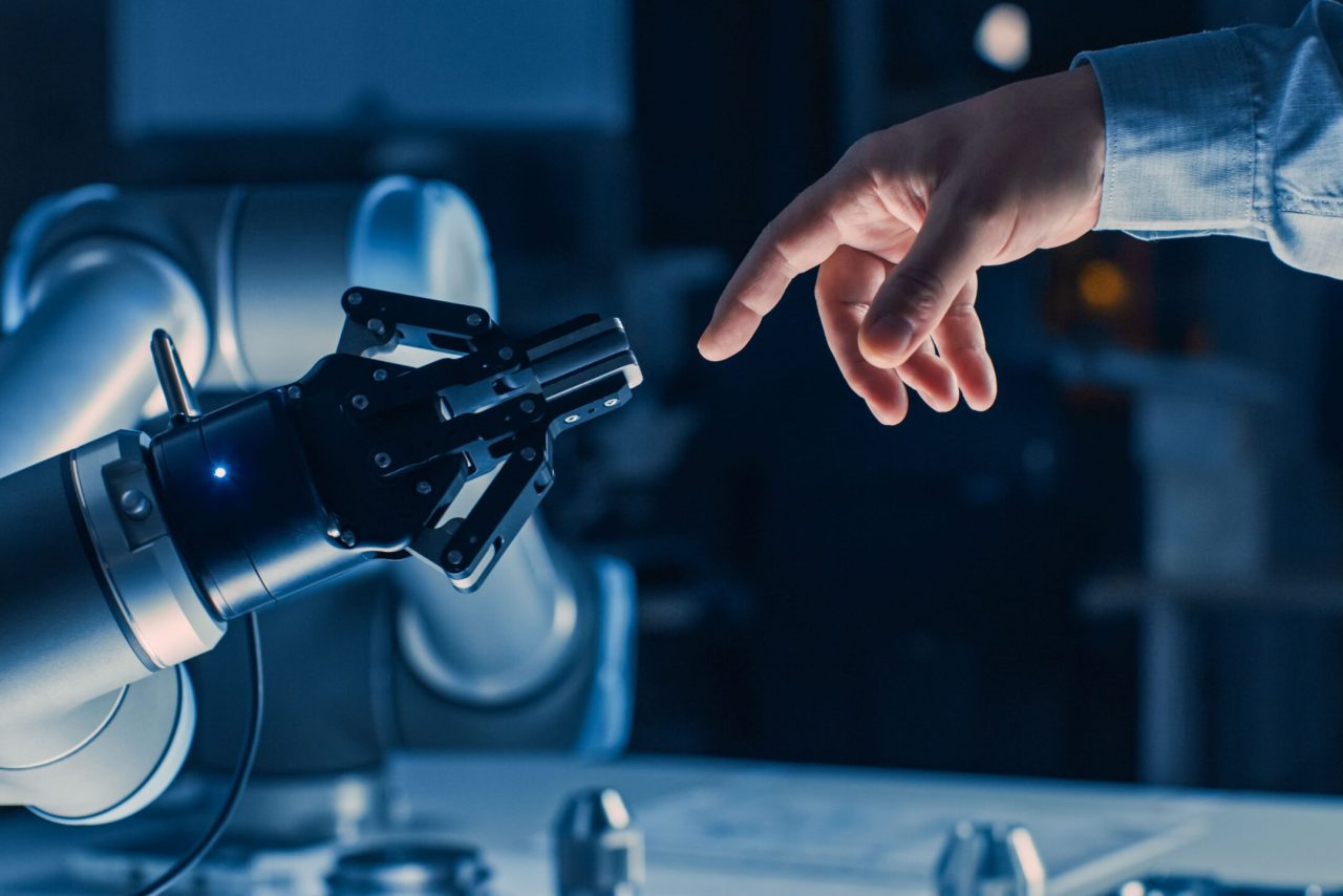 Human hand reaching a robotic hand, symbolising open innovation, collaboration and digital transformation in modern manufacturing.